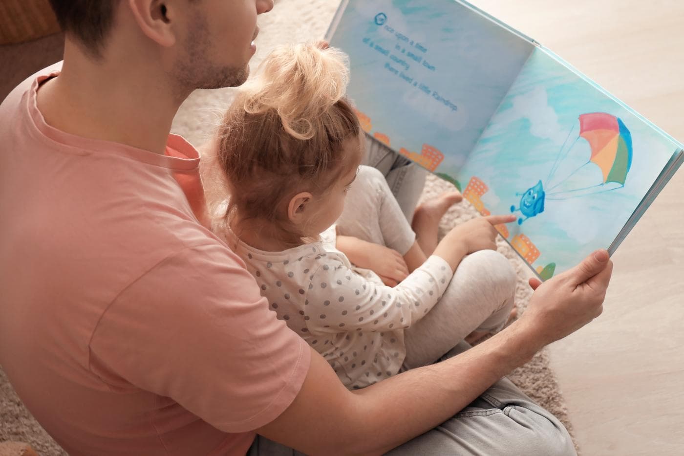 En vuxen och ett barn läser en bilderbok tillsammans på golvet
